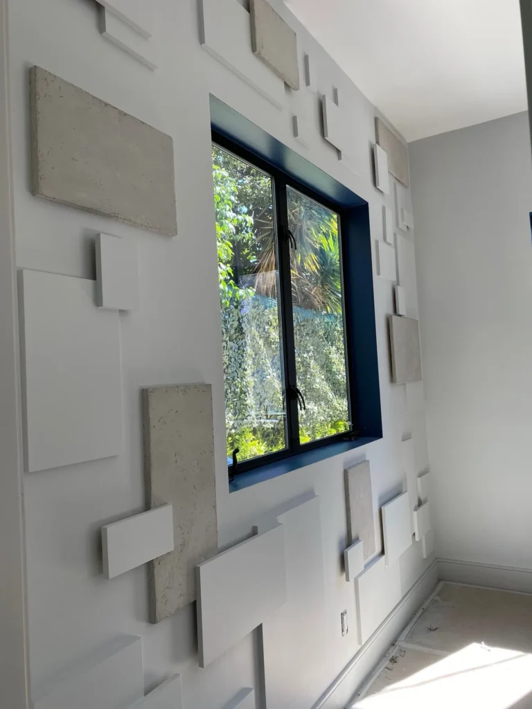 Layered geometric wall panels in light gray and wood tones framing a window