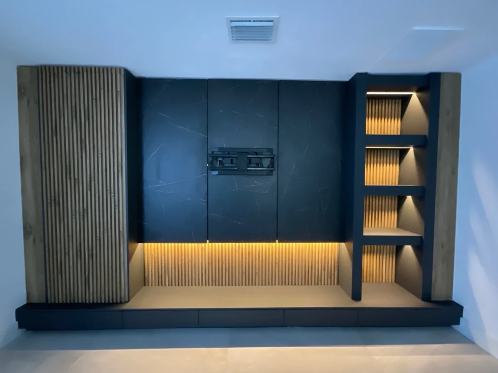 Custom media wall with white oak slats, matte black cabinets and warm LED shelf lighting