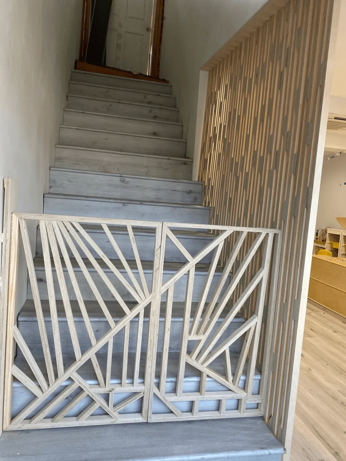 Staircase with vertical wood slats and a custom geometric railing at the landing